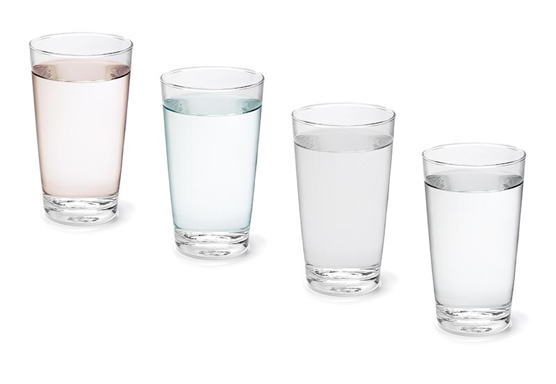 Four drinking glasses arranged in a row on a white background, filled with liquids of varying subtle tints.