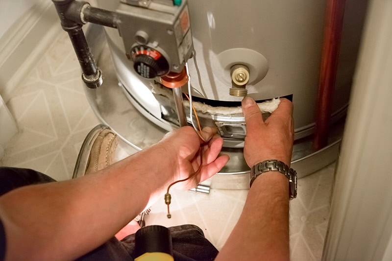 Man shines flashlight on hot water heater.