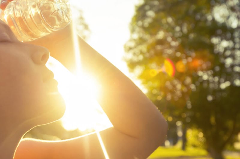 Woman using water bottle to cool down. Fitness and wellbeing concept with female athlete cooling down on a city street. She is holding a water bottle to her head to cool down. The sun is low creating long shadows and some lens flare. Copy space